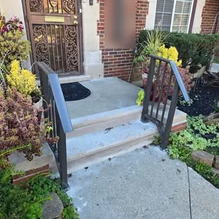 Black steel railings on both sides of the front steps of a brick home