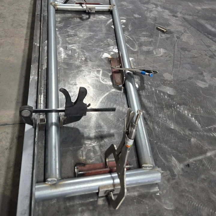 A steel tube frame held in welding clamps on the shop table